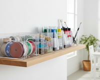 Clear storage bins holding organized craft supplies like ribbon, beads, and paint on a shelf